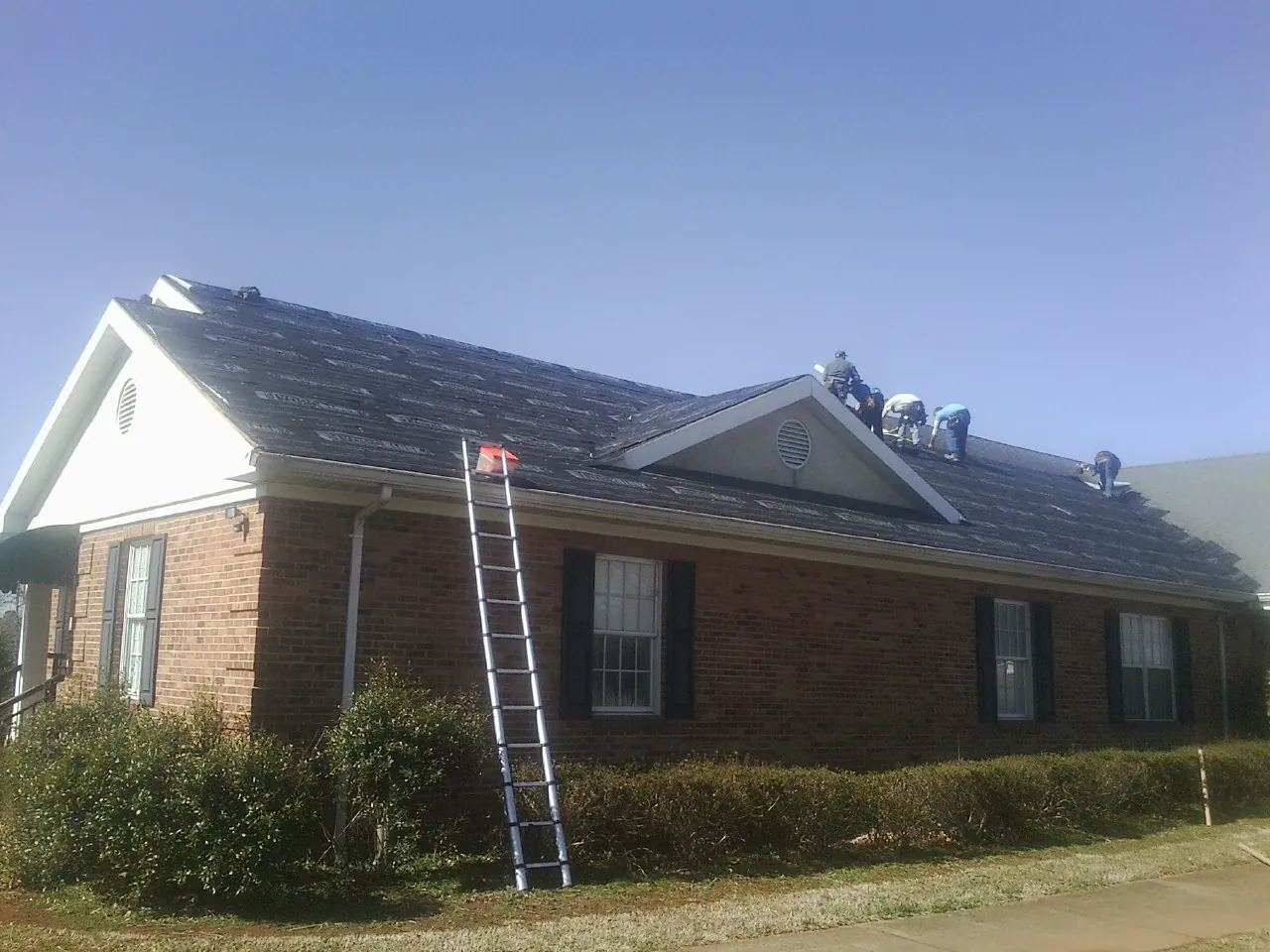 Crew tearing shingles off a brick ranch roof with a ladder set — Emergency Roof Repair work by our crew in Quinton