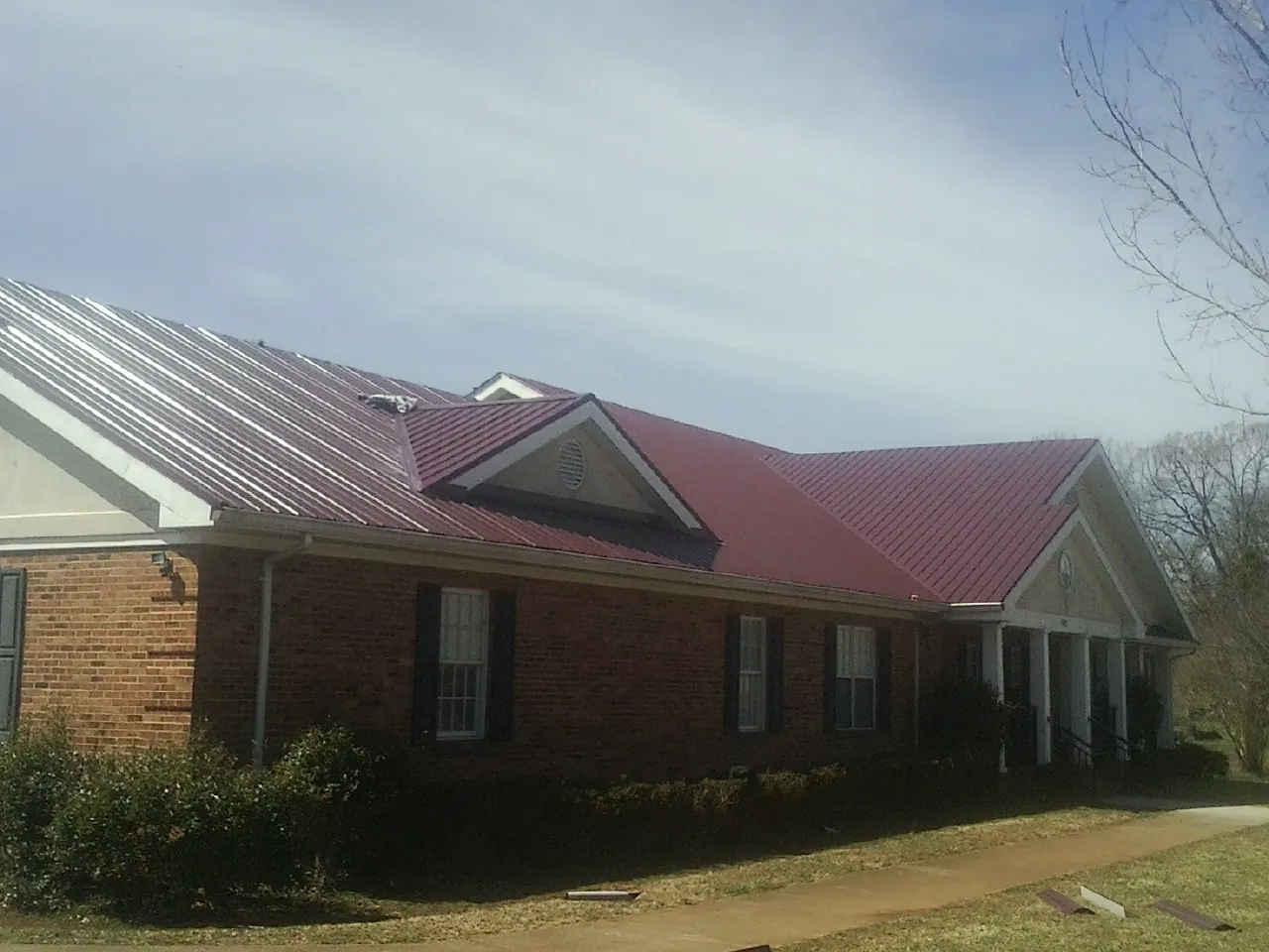 Red metal roof with gabled entries on a long brick building, from a Hail Damage Roof Repair job in Quinton