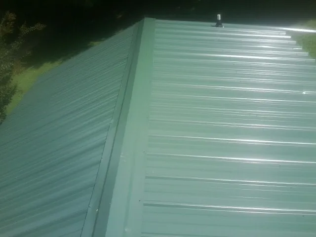 New green metal panels meeting at the ridge of a roof — Flat Roof Repair work by our crew in Quinton