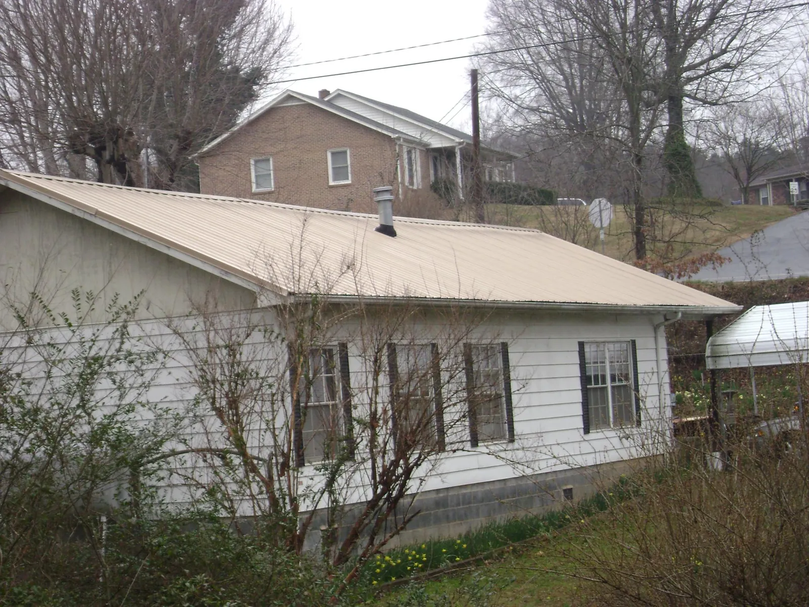 Tan metal roof on a white sided house set into a hillside — Commercial Roofing by Roofing Brothers in Quinton