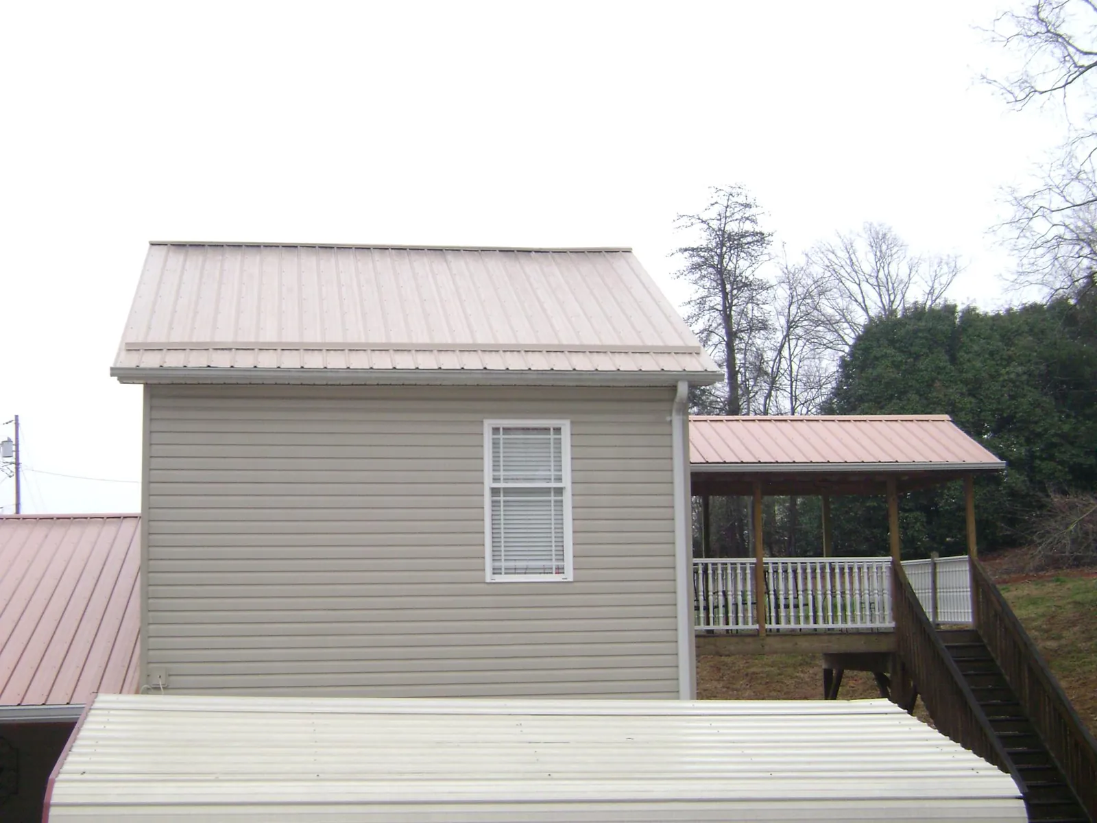 Tan metal roofs on a two story addition and attached porch, from a Roof Replacement job in Quinton